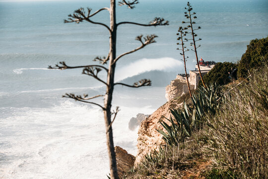 View of people watching surfers on Farlo de Nazar&egrave;, as they ride the waves, Nazar&egrave;, Estremadura, Portugal.