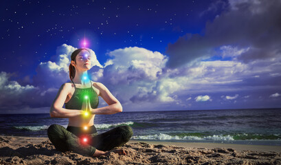 7 chakras. A woman meditates in the lotus position on the background of dark night blue sky and...