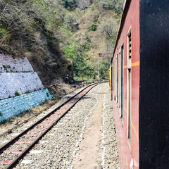 Obraz premium Toy Train moving on mountain slopes, beautiful view, one side mountain, one side valley moving on railway to the hill, among green natural forest. Toy train from Kalka to Shimla in India, Indian Train