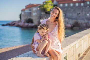 Fototapeta na wymiar Mother and daughter tourists on background of beautiful view St. Stephen island, Sveti Stefan on the Budva Riviera, Budva, Montenegro. Travel to Montenegro concept