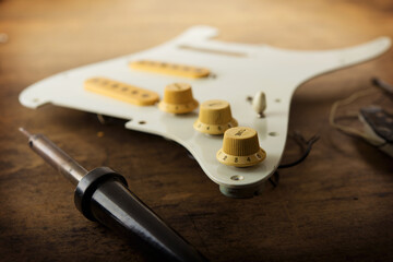 Electric guitar repair and maintenance. Pickguard section of an electric guitar on work bench with...