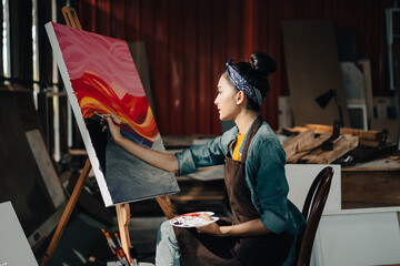 Asian Female Artist Draws create art piece with palette and brush painting at studio.