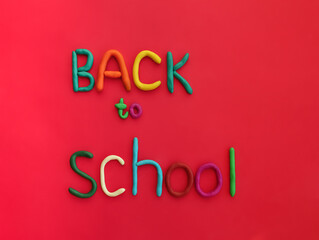 letters made of multi-colored plasticine back to school on red background