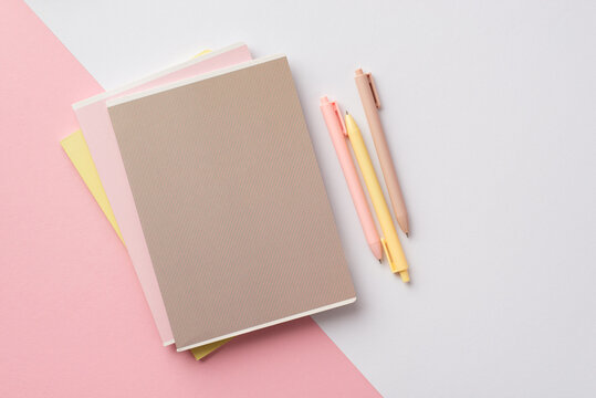 Back to school concept. Top view photo of school supplies stack of notebooks and pens on bicolor pink and white background