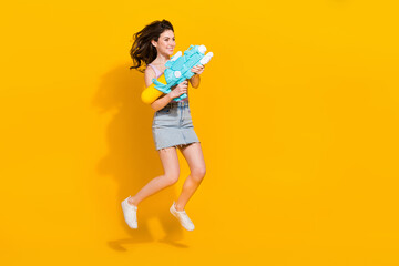 Full body photo of excited active pretty girl jump hold water gun isolated on yellow color background