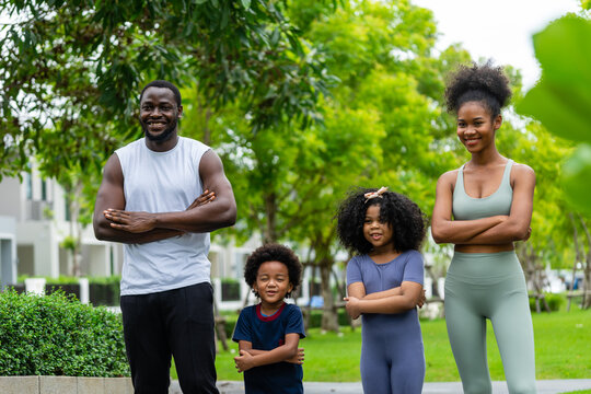 A family of black Americans and their son and daughter in sportswear line up to take pictures, smiling cheerfully at the camera.