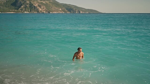 slow motion of enjoyed athletic man going out of turquoise water of mediterranean sea in Oludeniz Beach in Aegean Sea after swimming. Summer tourist Season Fethiye, Mugla Turkey