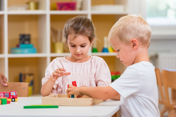 A couple of children are playing with colorful wooden toys at kindergarten. They are concentrated on their play.