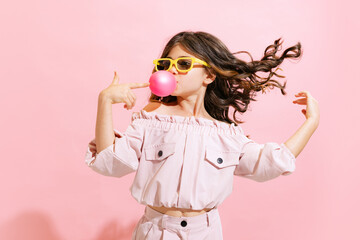 Fashionable little girl, kid posing isolated over pink color background. Concept of children emotions, fashion, happy childhood, beauty, school and ad