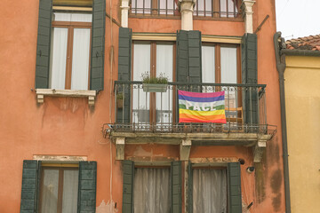 Fototapeta na wymiar Rainbow peace flag exposed on city house facade to support stop war in Ukraine. 