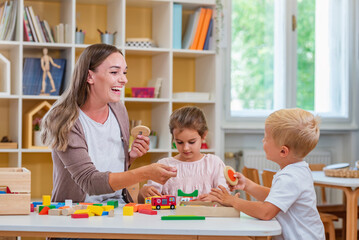 Kindergarten teacher playing together with children in the colorful preschool classroom. Mother playing with children.