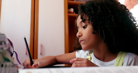 Mixed race girl writing notes doing homework at home. Little girl kid concentrated studying