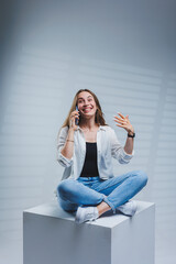 Young woman with long brunette hair, wearing a white shirt and jeans, talking on the phone. A woman in jeans and a plain white shirt with a mobile phone. White background, copy space.