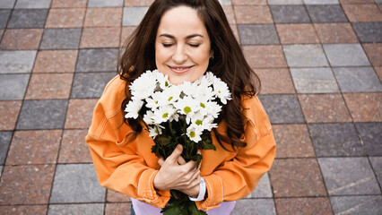 Fototapeta premium high angle view of happy woman with closed eyed smelling white flowers outside.