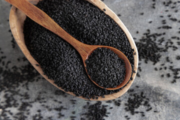 Indian spice Black cumin (nigella sativa or kalonji) seeds in bowl with spoon on wooden table top...