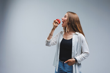 Cute brunette woman in white shirt holding red apple in hand standing on isolated white background...