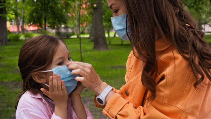 Obraz premium mother adjusting blue medical mask on daughter in park.