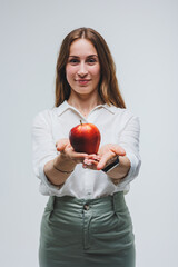 Smiling woman holding a red apple. Beautiful brunette in a white shirt. Healthy plant food and vitamins. White background.