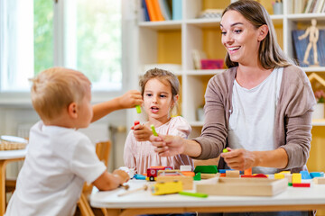 Fototapeta premium Kindergarten teacher playing together with children in the colorful preschool classroom. Mother playing with children.
