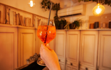 A woman hand is holding a glass full of Aperol spritz cocktail inside a vintage bar. Drinks and...