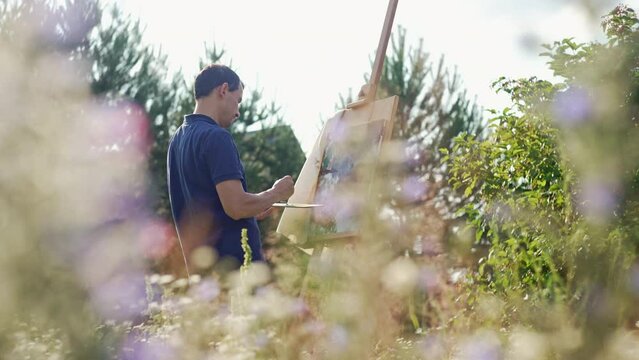 The artist's hand paints a picture on the lawn with flowers. Man Artist, Inspiration in Nature. High quality 4k footage