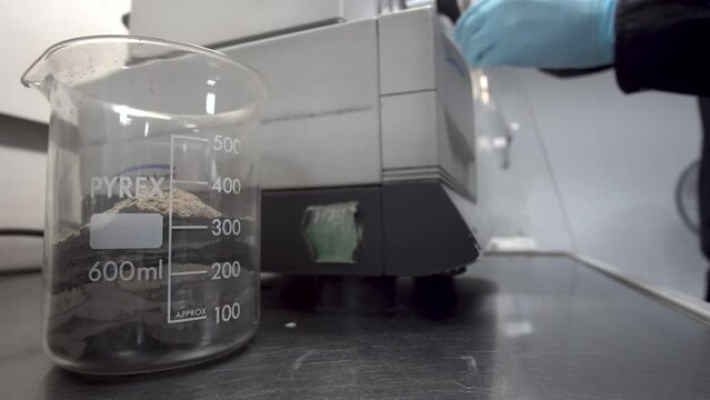 Lab worker prepares ore sediment sample for analysis with glass beaker