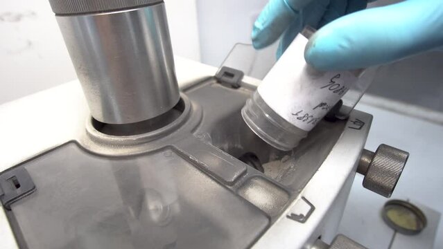Man with gloves inserts powder into a milling machine in a research lab