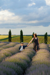 Mom and son walk holding hands in a lavender field with a beautiful landscape and sky