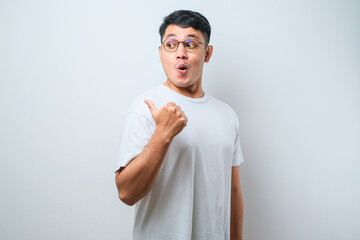 Young asian man surprised pointing with hand finger to the side, open mouth amazed expression.