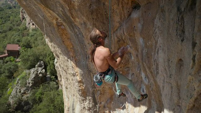 muscular man Rock climber hangs on rope on overhanging crag, chalks his hands and gets ready to climb next pitch on challenging route on big rock wall in Turkey. 4k slow motion