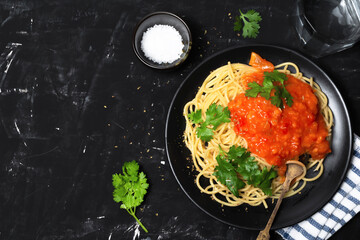 Pasta with tomato sauce in black dish on black wood background