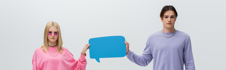 Young couple in sweatshirts holding speech bubble isolated on grey, banner.