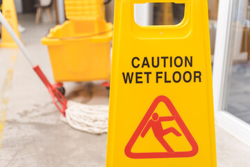 A Caution Wet Floor sign placed to warn passersby while wiping a wet concrete floor with a string...