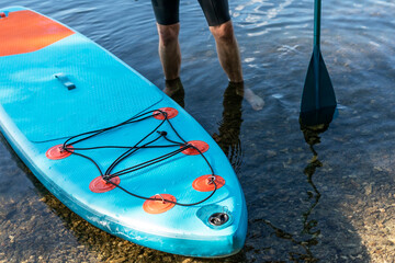 Man faceless with stand up paddleboard blue SUP on the water lake with paddle male legs active...