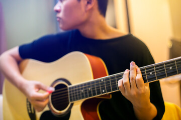 Selective focus to finger of Asian teenage playing acoustic classical guitar.