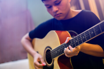 Selective focus to finger of Asian teenage playing acoustic classical guitar.