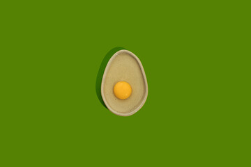 Avocado shaped ceramic plate with yellow raw egg yolk on a bright green color background with copy space. Healthy dieting idea.