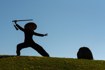 Asian woman with sword practicing taijiquan at sunset, chinese martial arts, healthy lifestyle concept.