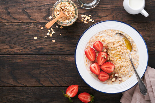 Oatmeal. Bowl of oatmeal porridge with strawberry, almond and milk on old wooden dark table background. Top view in flat lay style. Natural ingredients. Hot and healthy breakfast and diet food.