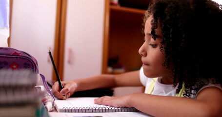 Smart concentrated little school girl doing homework writing notes