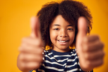 Studio Portrait Of Smiling Young Boy Making Thumbs Up Gesture Shot Against Yellow Background