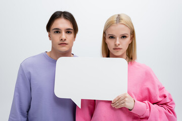Young couple in sweatshirts holding white speech bubble isolated on grey.