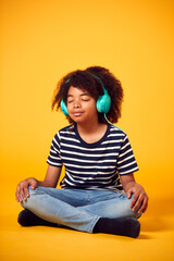 Studio Shot Of Boy With Eyes Closed Listening To Music On Headphones Against Yellow Background