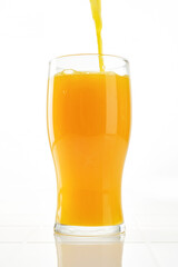 Filling a glass with orange juice. Orange juice pouring into drinking glass on white background. Shallow depth of field