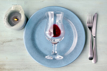Empty blue plate with glass of red wine, cutlery and burning candle on blue wooden table