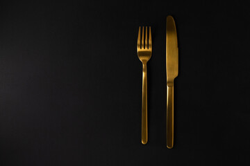 Golden fork and knife on the black background.
