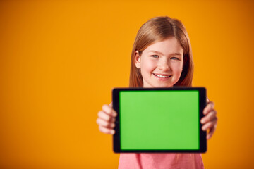 Fototapeta na wymiar Studio Portrait Of Girl Using Digital Tablet With Green Screen Against Yellow Background
