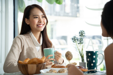 Two young Asian women friends talking at a coffee shop