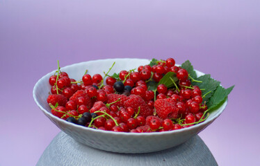 Plate with raspberries, black and red currants on a purple background