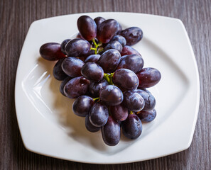 Ripe grapes in a white plate on a wooden table, top view.  A bunch of grapes in a plate on the table. Wine grapes. Fresh fruits and berries.